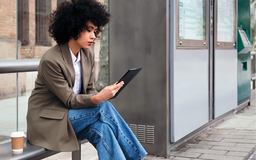 Frau mit Tablet in der Hand draußen beim Kaffeetrinken
